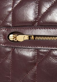 Burgundy leather bag featuring quilted pattern, gold zipper hardware, and contrast stitching. Surface has a slightly textured finish.