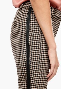 Jupe crayon à carreaux en noir, beige et blanc; présente une coupe slim avec une bande latérale noire et un tissu texturé.