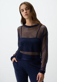 Navyblauw gaas lange mouw top met een losse pasvorm, met een ronde halslijn en een gelaagd ontwerp. De textuur is open gebreid met een ruitpatroon.