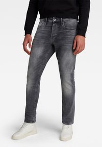 Grå denimjeans med slim fit och blekt tvätt; har bälteshällor, framfickor och knappstängning. Matchas med vita högskaftade sneakers.