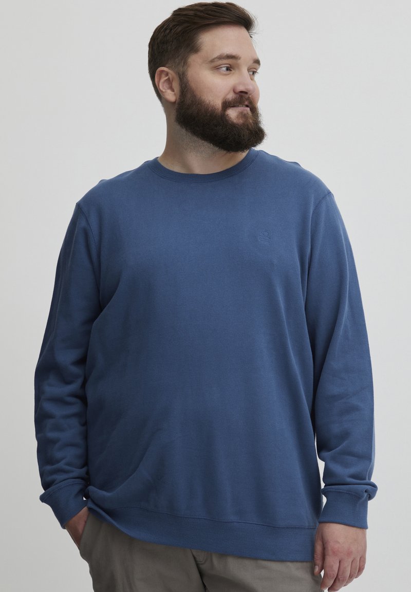 Sudadera azul de cuello redondo hecha de tela suave con mangas largas, que presenta un cuello y puños acanalados, corte relajado, diseño simple, sin patrones.