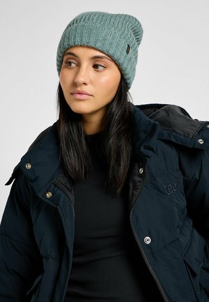 Dziana czapka beanie w miękkim, stonowanym odcieniu niebieskiego; prążkowana faktura; metki po boku. Nosi się z czarną kurtką puchową na zamek i dopasowanym topem.