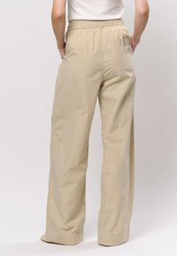 Beiget leveälahkeiset housut, joissa on joustava vyötärönauha, sileä pinta ja takataskun yksityiskohta. Housuissa on rento istuvuus ja hillitty kiilto.