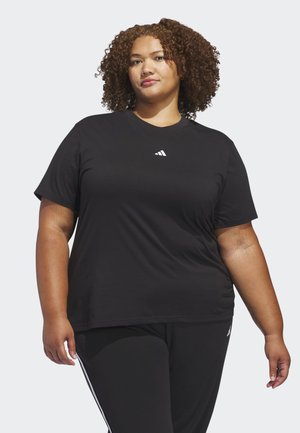 Kirtsutega naine, kes kannab musta Adidas t-särki ja musta pükse valgete triipudega, lihtsal heledal taustal.