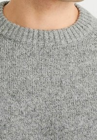 Pull gris clair en maille avec un col rond côtelé. Le tissu texturé présente des variations subtiles et une apparence douce.