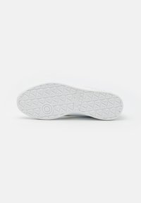 Semelle de sneaker blanche avec un motif texturé, comportant des formes géométriques et un emblème circulaire. Fini lisse sans couture visible.
