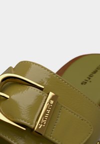 Sandale en cuir verni vert avec une boucle en métal doré. Elle comporte une semelle moulée et un logo visible sur la semelle intérieure.