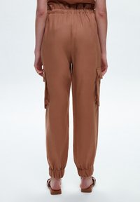 Pantalon cargo marron avec une coupe décontractée, taille élastique, poches latérales et ourlets élastiques. Texture lisse, tissu léger.