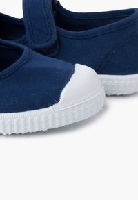 Scarpe da tela navy con copertura in gomma bianca sulla punta e suola bianca testurizzata. Presentano una fascia in velcro per una calzata sicura.