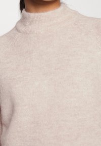 Ljust rosa, mjuk stickad tröja med hög hals, raglanärmar och en slät yta. Enkel design utan synliga mönster eller detaljer.