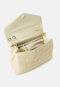 Μπεζ πλεκτή τσάντα με υφαντή εξωτερική επιφάνεια, χρυσές λεπτομέρειες και κλείσιμο με κουμπί. Ο εσωτερικός χώρος περιλαμβάνει διαμερίσματα και μια τσέπη με φερμουάρ.