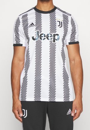 Homme portant un maillot de football Juventus noir et blanc avec le logo Jeep et la marque Adidas, avec un pantalon Adidas noir assorti.