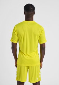 Felgeel sportshirt met korte mouwen, ronde halslijn en bijpassende shorts met witte chevronaccenten aan de zijkanten.