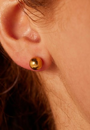 Boucle d'oreille en or présentant un design rond et lisse. La boucle est positionnée sur un lobe, mettant en valeur sa surface réfléchissante.