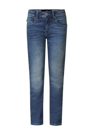Personne portant un t-shirt blanc uni à manches courtes, un jean bleu clair et des baskets blanches sur un fond blanc uni.