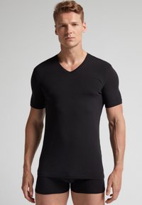 Svart kortärmad T-shirt med V-hals i en slim-fit design, tillverkad av mjukt och elastiskt material, tillsammans med svarta tajta shorts.
