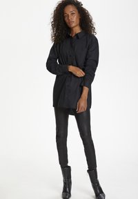 Black button-up shirt with a collar and single chest pocket, paired with form-fitting black leather pants and ankle boots.