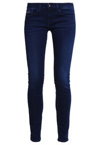 Vaqueros ajustados azul oscuro hechos de denim, que presentan un diseño clásico de cinco bolsillos, pasadores para cinturón y un cierre frontal con cremallera y un botón de metal.