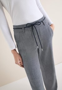 Pantalon gris texturé avec une taille à cordon et des poches, agrémenté d'un accent bleu marine sur le cordon. Associé à une chemise blanche à manches longues.