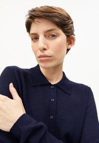 Marineblauer Pullover mit Kragen und langen Ärmeln, der eine durchgehende Knopfleiste und eine glatte Textur aufweist. Die Knöpfe sind dunkelblau und passen zum Stoff.