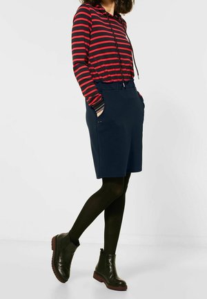 Sudadera de rayas rojas y marinas con cordones, combinada con una falda de cintura elástica en color marino con bolsillos. Llevada con medias negras y botas de tobillo.
