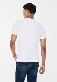 Vit bomull T-shirt med rullade ärmar, rund hals och avslappnad passform, tillsammans med mörkblå denimjeans med standard bakfickor.