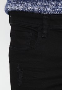 Jeans de denim negro con diseño clásico de cinco bolsillos, trabillas para cinturón, ligero detalle desgastado y textura suave.