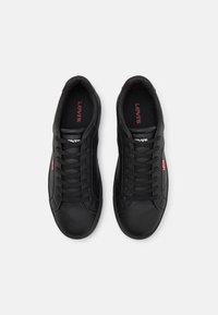 Paire de baskets noires à lacets Levi’s vues de dessus sur fond blanc, avec le logo rouge Levi’s sur les semelles intérieures et les étiquettes latérales.