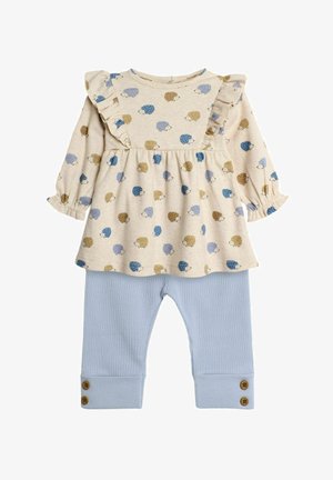 Tenue beige clair composée d'un haut à manches longues avec des accents de volants et des motifs de hérisson, associée à un pantalon bleu clair côtelé avec des détails de boutons.