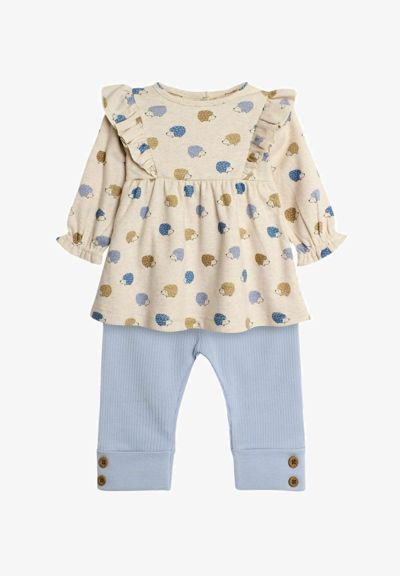 Conjunto de color beige claro que incluye una blusa de manga larga con acentos de volantes y patrones de erizos, combinada con pantalones de canalé azul claro con detalles de botones.