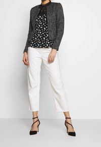 Czarna i biała, teksturowana kurtka na kwiecistej czarnej bluzce, w połączeniu z białymi spodniami 3/4 i czarnymi szpilkami.