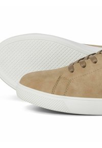 Beige Leder-Sneaker mit abgerundetem Zehenbereich, kontrastierenden braunen Schnürsenkeln und einer strukturierten weißen Gummisohle mit Rautenmuster für besseren Halt.