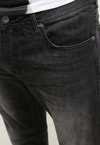 Černé džíny z denimu s klasickým designem pěti kapes, jemným vyblednutím a kontrastním prošíváním. Materiál působí měkce a hladce.