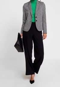 Blazer gris à chevrons avec deux boutons noirs, associé à un col roulé vert et un pantalon noir large taille haute. Sac à main noir inclus.