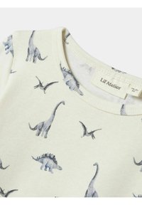 Kreminės spalvos medvilninė marškinė su apvaliu iškirpimu, su dinozaurų raštu pilkose atspalviuose. Etiketėje užrašyta "Lil'Atelier."