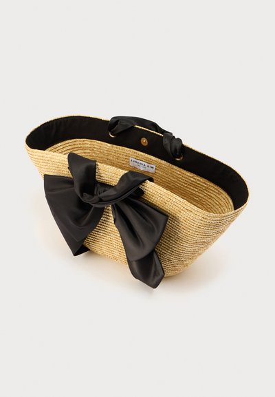 Τσάντα χειρός από άχυρο με επίπεδο, οβάλ σχήμα. Διαθέτει μεγάλο μαύρο σατέν φιόγκο και μαύρη υφασμάτινη επένδυση. Μεταλλικό κουμπί κλεισίματος στο πάνω μέρος.