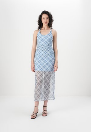 Blauwe geruite maxi-jurk met racerback ontwerp, doorschijnend ondergedeelte en geraffineerde details op de taille; gecombineerd met zwarte sandaaltjes met bandjes.