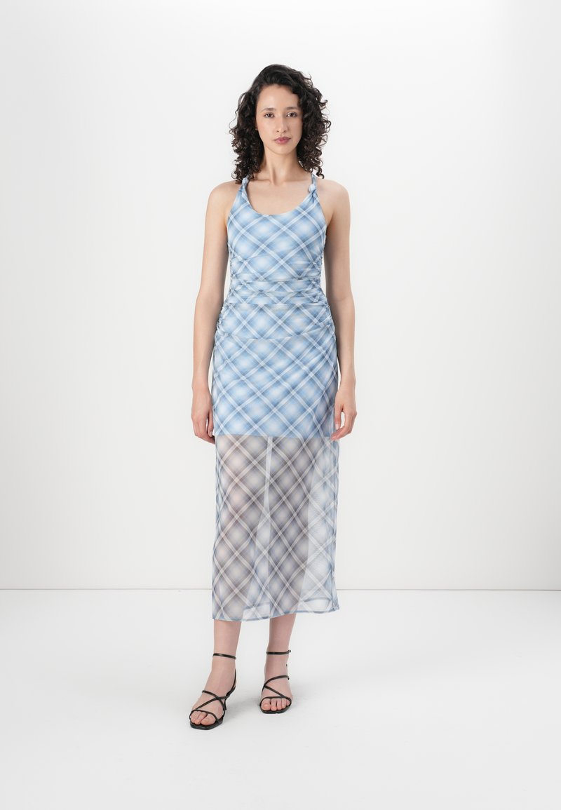 Blauwe geruite maxi-jurk met racerback ontwerp, doorschijnend ondergedeelte en geraffineerde details op de taille; gecombineerd met zwarte sandaaltjes met bandjes.