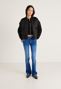 Fekete bomber dzseki cipzárral, két elülső zsebbel, kék, bővülő szárú farmerral és fekete mintás cipőkkel párosítva. Egyszerű, rövidített fekete felső alatta.