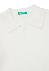 Pletený bílý polo svetr s V-výstřihem a žebrovaným límcem; obsahuje štítek s nápisem "United Colors of Benetton" v zelené barvě.