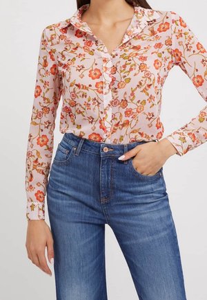 Blusa floreale abbottonata di colore rosa chiaro, con motivi di fiori rossi e verdi, colletto classico e maniche lunghe, abbinata a jeans a vita alta.