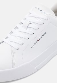 Weiße synthetische Sneakers mit flachen Schnürsenkeln, strukturiertem Obermaterial und gepolstertem Kragen. Verfügt über ein Logo an der Seite und eine feste Gummisohle.