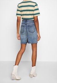 En person som bär en blå jeanskjol med bakfickor och mittslits, ihop med en kortärmad randig skjorta och vita klackade ankelskor.