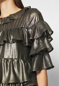 Metallinvihreä yläosa, jossa on useita frillikerroksia, röyhelökaula-aukko ja sileä, kiiltävä pinta.