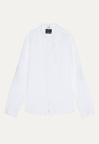 Camicia bianca a maniche lunghe con colletto alla cinese, etichetta di marca visibile e design semplice, stesa su uno sfondo chiaro.