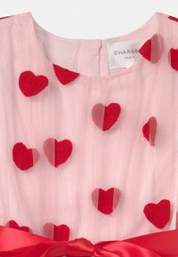 Różowa sukienka z tiulu z aplikacjami w kształcie czerwonych serc z filcu, okrągłym dekoltem i satynowym paskiem w talii z kokardą. Metka głosi "CHARABIA."