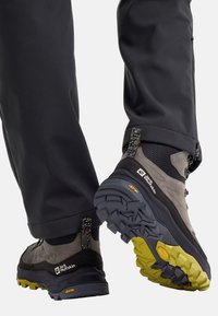 Scarponi da trekking con una tomaia in tessuto grigio e nero, suola gialla, suola con grip testurizzato e dettagli in contrasto. Presentano un tallone rinforzato e un design con lacci.