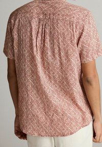 Chemise à manches courtes avec un motif en losanges rouge et crème. Caractéristiques : coupe décontractée, pli au dos et tissu léger avec une texture lisse.