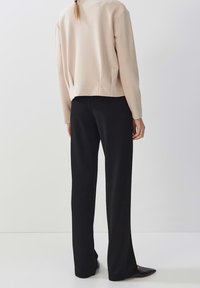 Beżowy sweatshirt z lekkim skróceniem i luźnym krojem, zestawiony z czarnymi spodniami o prostym kroju oraz czarnymi butami na szpic. Prosty design.