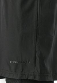 Musta urheilu takki, johon on käytetty sileää ja kevyttä kangasta. Varustettu neulotuilla reunoilla ja heijastavalla "ENDURANCE"-logolla.